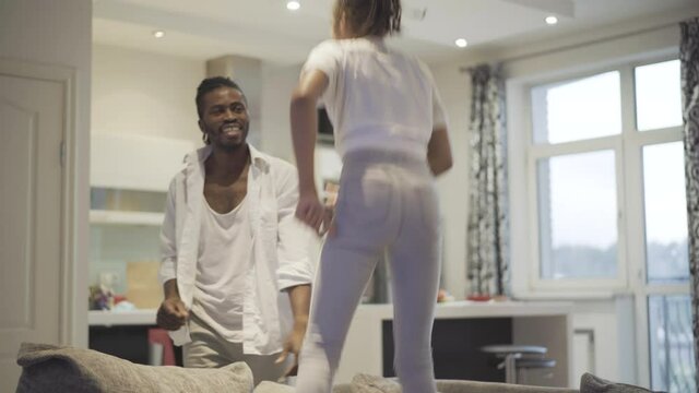 Positive African American father and daughter dancing and having fun at home. Joyful man and teenage girl enjoying weekends indoors. Leisure and lifestyle.