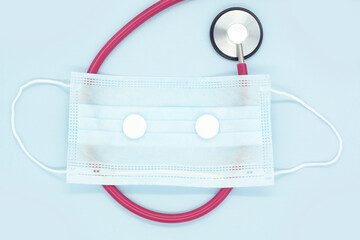 Protective face mask and stethoscope on blue background.