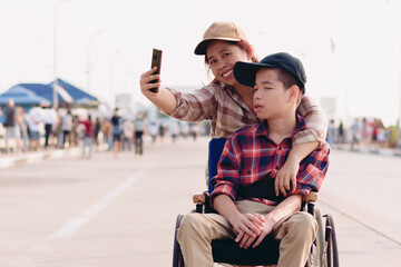 Obraz na płótnie Canvas Asian Disabled child on wheelchair and mother in the outdoors nature fun with selfie by smart phone,Life in the education age of special children,Happy disability kid travel in family holiday concept.