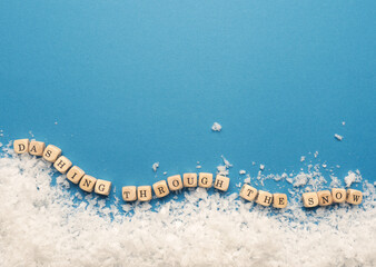 Small wooden block s with the inscription Dashing through the snow with snowflakes on a blue background