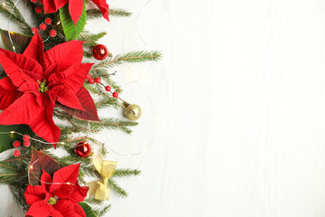 Flat lay composition with poinsettias (traditional Christmas flowers) and holiday decor on white wooden table. Space for text