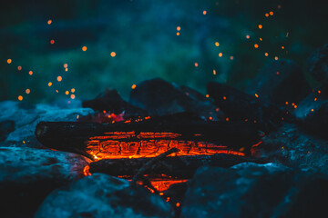 Vivid smoldered firewoods burned in fire closeup. Atmospheric background with orange flame of campfire. Wonderful full frame image of bonfire with glowing embers in air. Warm logs, bright sparks bokeh