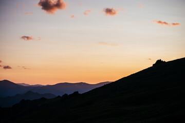 Warm gradient of dawn sky above layers of mountain and rock silhouettes. Vivid alpine landscape with dark rockies and orange sunrise sky. Minimalist highland scenery with silhouette of rocky mountains
