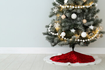 Decorated Christmas tree with red skirt indoors, space for text