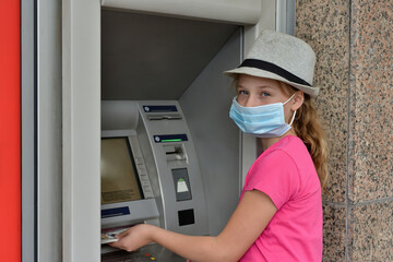 Fototapeta na wymiar A girl counts money in a protective mask during a covid quarantine near an ATM