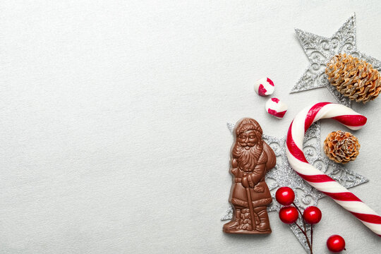 Flat lay composition with chocolate Santa Claus, candy cane and Christmas decorations on light grey background. Space for text