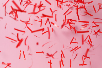 Shiny red confetti falling down on pink background
