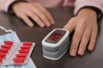 Woman measuring oxygen level with modern fingertip pulse oximeter at grey table, closeup