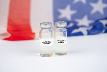 Two bottles with covid-19 vaccine. US flag on background