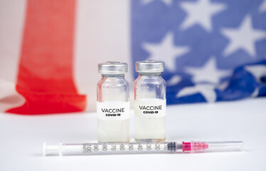 Two bottles with covid-19 vaccine. US flag on background