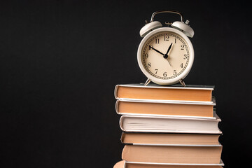 The alarm clock stands on a stack of books on a black background. Training concept and preparation for work