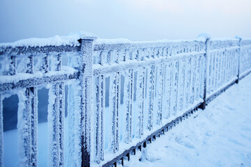 Metal fence covered with snow and frost in the city park. Extremely cold winter