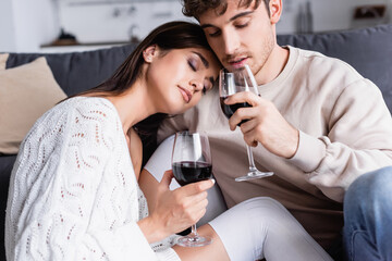 Brunette woman holding glass of wine near boyfriend at home