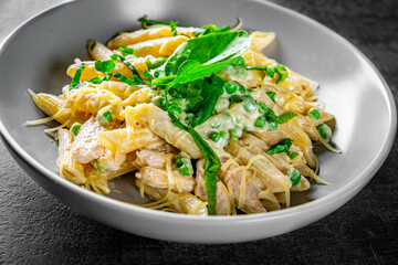 Penne pasta with chicken meat, cream sauce and cheese in a bowl on Dark grey black slate background