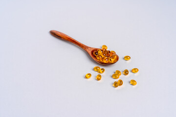 Yellow capsules of vitamin D or fish oil on a wooden spoon