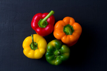 Bright multi-colored bell peppers lie on a black modern concrete background. Red peppers, orange, yellow and green bell peppers. Flat lay, top view, mock up