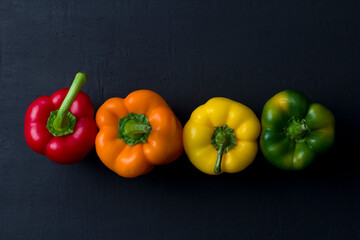 Bright multi-colored bell peppers lie on a black modern concrete background. Red peppers, orange, yellow and green bell peppers. Flat lay, top view, mock up