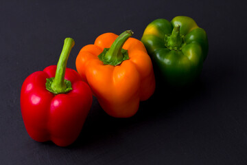 Bright multi-colored bell peppers lie on a black modern concrete background. Red peppers, orange, yellow and green bell peppers. Flat lay, top view, mock up