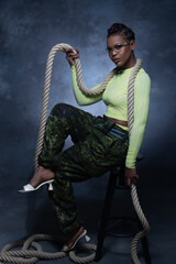 Sexy girl wearing military style pants and neon underwear posing with rope and looking into the...