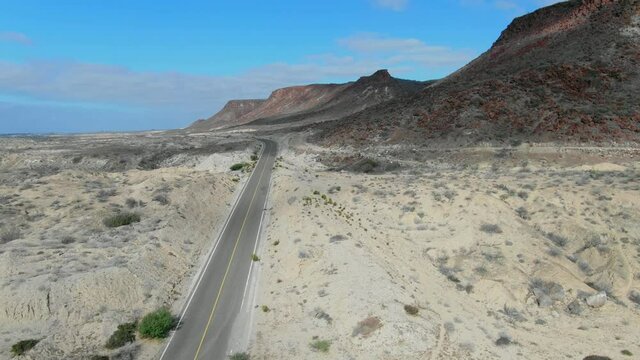 Aerial view moving forward shot, highway besides a red rocky mountain in La Purisima Baja California sur, Mexico, blue sky in the background.
