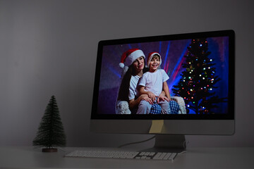 Mother and son in santa claus hats congratulate merry christmas on a video call on a computer