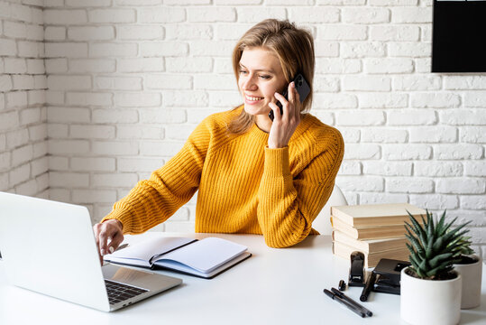 Young Woman In Yellow Sweater Using Laptop And Calling On The Phone