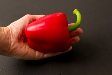 Hand holds red bell pepper close-up on black background