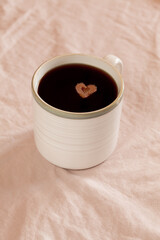 White cup of coffee with heart shaped sugar on pink textile background. Concept of love
