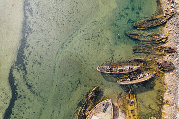 Ship graveyard in Teriberka on Barents Sea coast, aerial top down view. Old wrecked fishing boats in water on shore. Texture of sea bottom with copy space. Kola Peninsula, Murmansk Oblast, Russia
