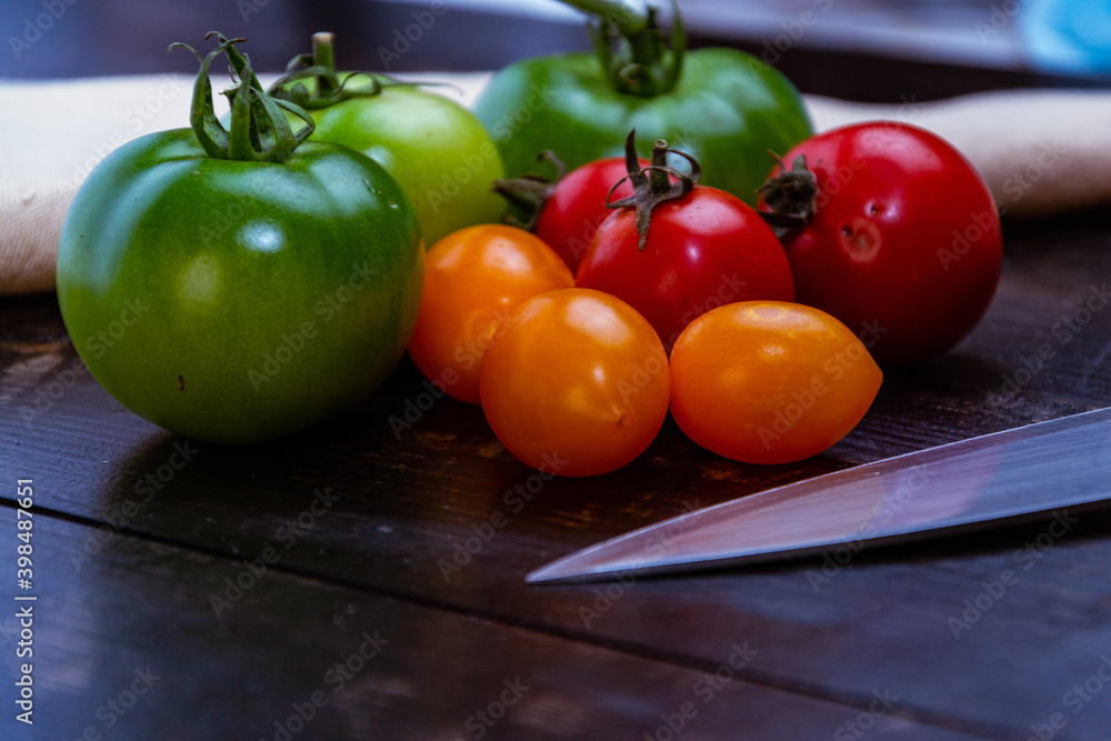 Wall mural Closeup shot of ripe and unripe tomatoes with knife and napkin on a wooden table