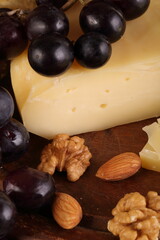 Gruyere cheese on a wooden table with grapes, nuts and olive oil