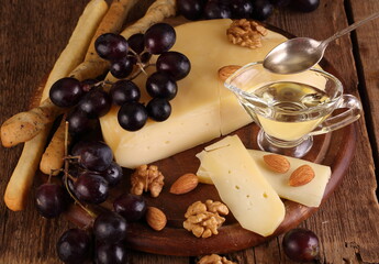 Gruyere cheese on a wooden table with grapes, nuts and olive oil