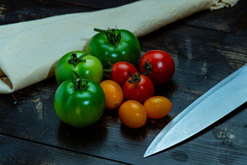 High angle shot of ripe and unripe tomatoes with knife and napkin on a wooden table