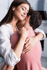 Young woman embracing boyfriend with closed eyes at home