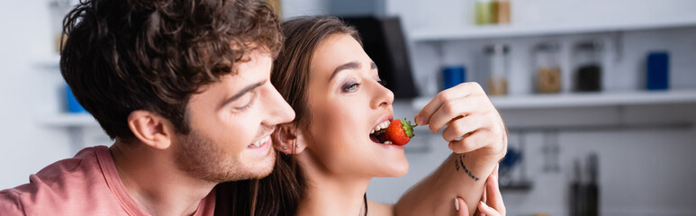Smiling man feeding girlfriend with fresh strawberry, banner