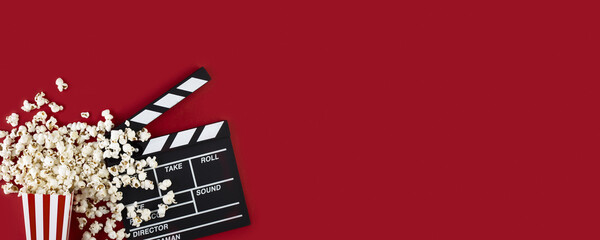 Watching movie with popcorn and clapperboard on red background. Movie goers accessories, cinematography concept. Long wide banner with copy space