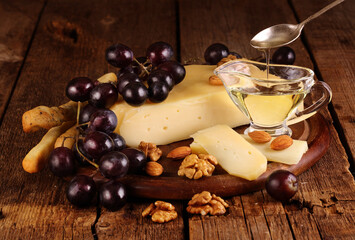Gruyere cheese on a wooden table with grapes, nuts and olive oil