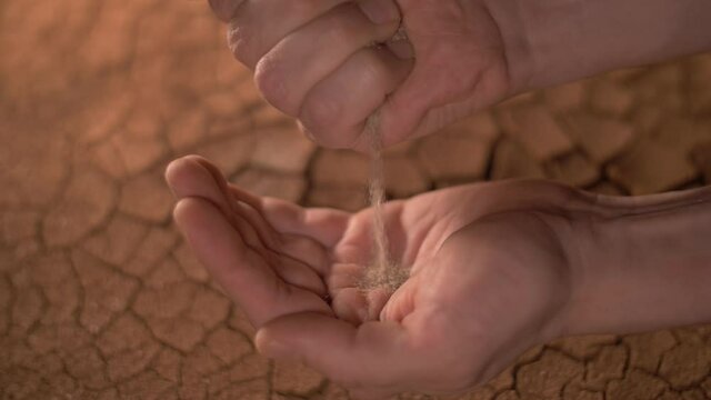 cracked soil in a desert drying out. drought concept, sand in hands, cracked earth on the background. climate change, global warming, water scarcity.