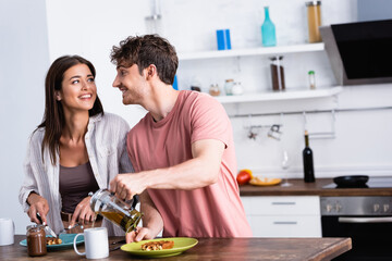 Smiling man pouring tea near girlfriend cutting waffle on kitchen table