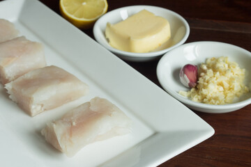 Close-up of a hake fillet with various natural ingredients such as garlic and butter in the background. Fresh fish for cooking.