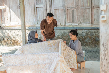 Fototapeta na wymiar portrait man checking batik result on a white cloth making by womens