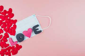 Red hearts, the word LOVE and a medical face mask on a pink background. Flat lay, copy space