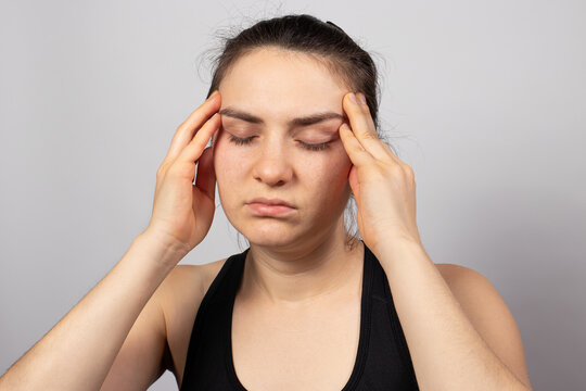 A Tired Woman Holds Her Head With Her Hand, Her Head Hurts. Brain Vascular Spasm, Hypertension, High Blood Pressure After Stress At Work. Fatigue And Excruciating Headache