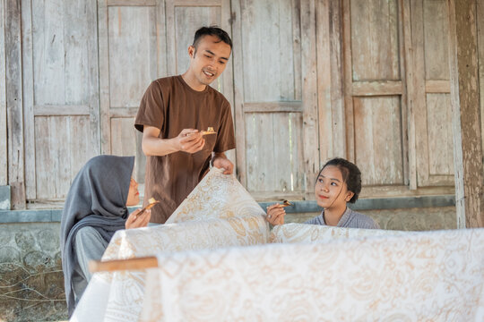 a man who teaches both women how to use canting for the draw batik