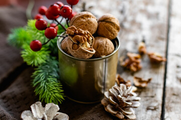 Walnuts in a tin, whole and split, next to the filling and shell. Presented in a New Year's composition with cones, red berries and a sprig of a Christmas tree. Home storage of winter preparations