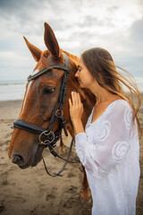 Fototapeta premium Portrait of beautiful woman and brown horse. Caucasian woman hugging and stroking horse. Love to animals. Beach in Bali, Indonesia