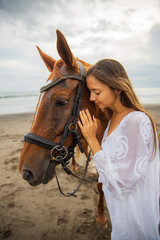 Fototapeta premium Portrait of beautiful woman and brown horse. Caucasian woman hugging and stroking horse. Love to animals. Beach in Bali, Indonesia