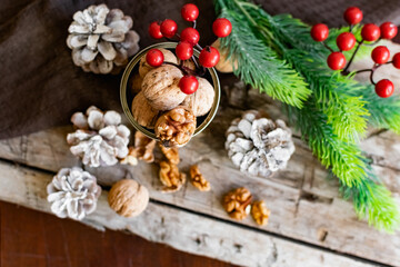 Walnuts in a tin, whole and split, next to the filling and shell. Presented in a New Year's composition with cones, red berries and a sprig of a Christmas tree. Home storage of winter preparations