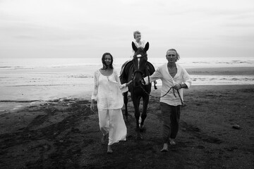 Monochrome. Little pretty girl on a horse. Parents leading horse by its reins on the beach. Horse riding. Family concept. Black-white photo. Summer holidays. Bali, Indonesia