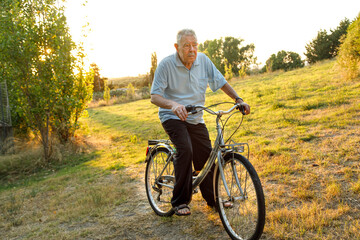 Signore ottantenne sta in sella alla sua bicicletta in un prato verde al tramonto